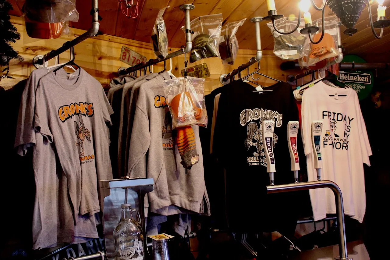 Gronk's Trading Post shirt and hoodie racks against wood paneling